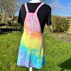 pinafore dress tie dyed in a pale rainbow colourway with pastel pink, orange, yellow, green, turquoise and purple.
