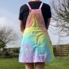 pinafore dress tie dyed in a pale rainbow colourway with pastel pink, orange, yellow, green, turquoise and purple.