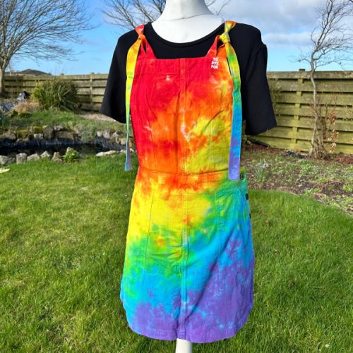 pinafore dress tie dyed in a rainbow colourway with red, orange, yellow, green, turquoise and purple.