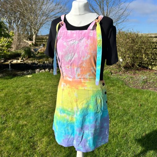 pinafore dress tie dyed in a pale rainbow colourway with pastel pink, orange, yellow, green, turquoise and purple.